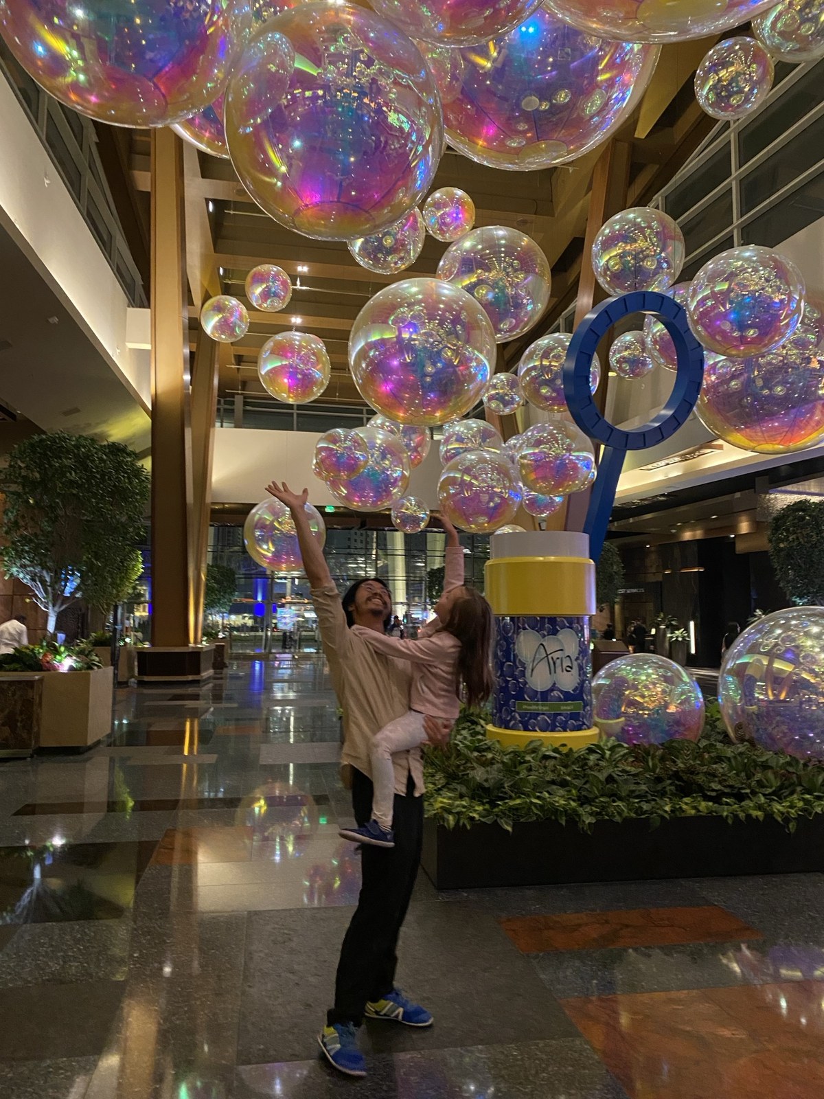 Alex lifting his daughter beneath iridescent balloons.